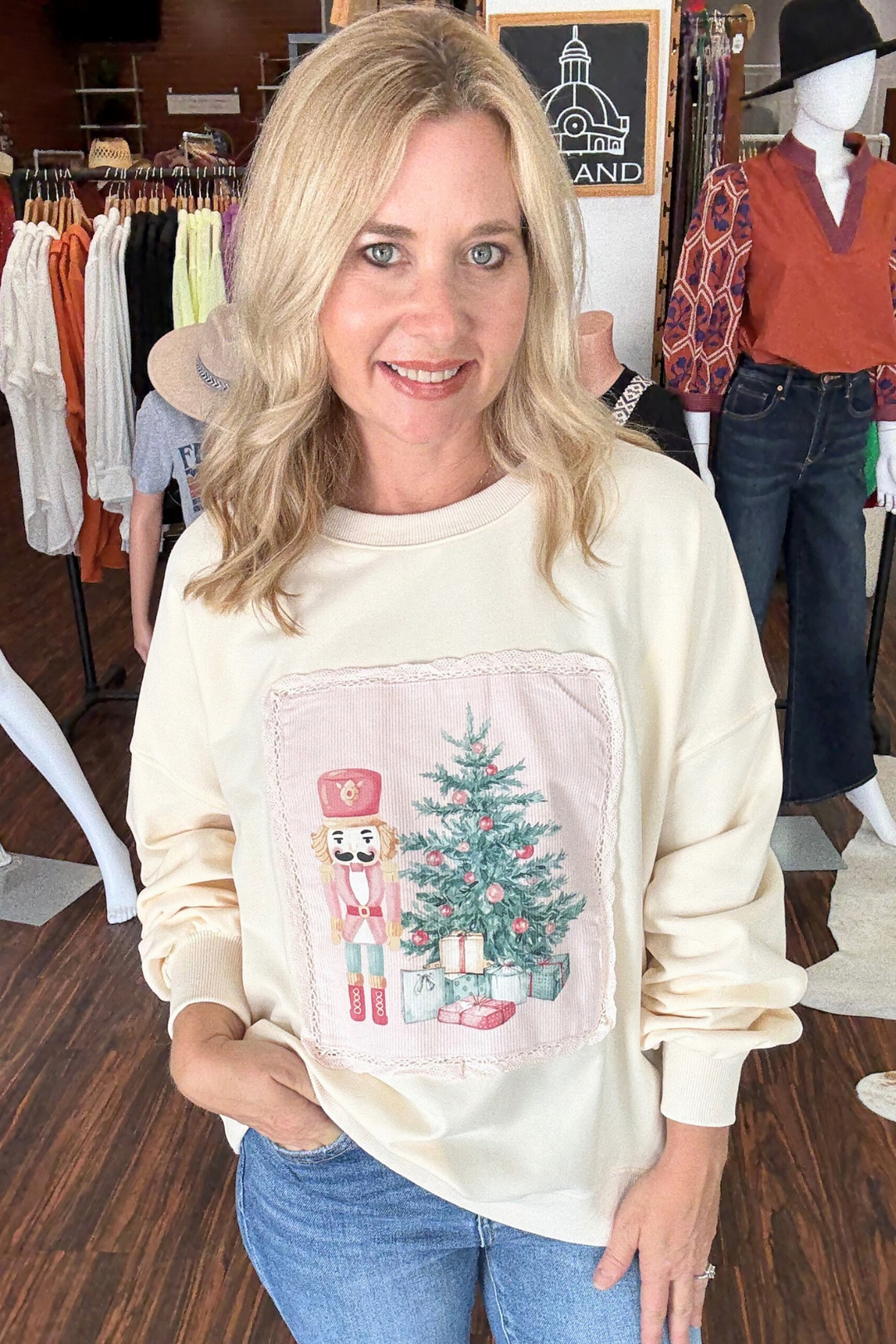 Soft oversized cream sweatshirt features a large front patch showcasing a festive nutcracker and Christmas tree, enhanced by delicate scalloped lace details. 