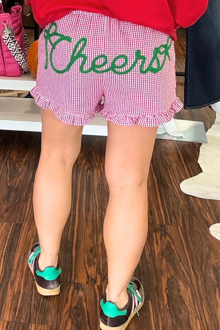 
These gingham shorts combine classic red and white print with a playful ruffle hem for a fresh, modern look. The elastic waist ensures comfort and a perfect fit, while the bold "Cheers" chenille lettering across the back. 