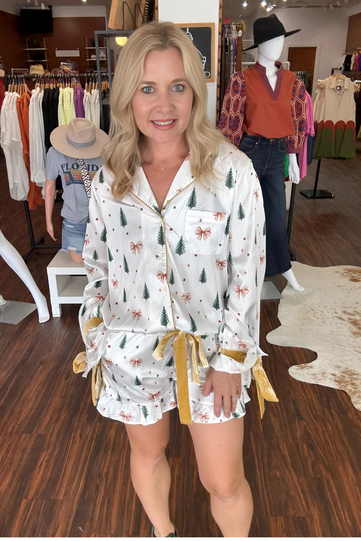 Relax in style this holiday season with the Gold Bow and Christmas Tree Satin Pajama Set. The white long-sleeve top features festive gold bows and Christmas tree prints, paired perfectly with matching shorts accented by a luxurious gold velvet tie