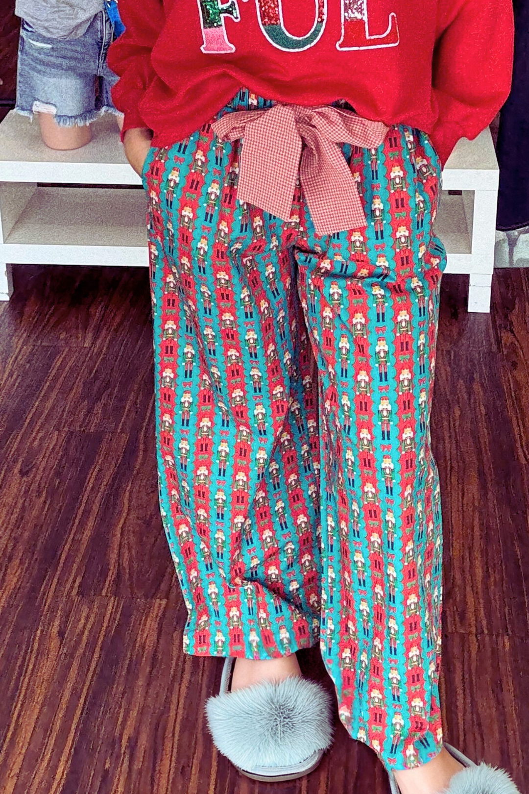 Holiday Toy Soldier Cotton Pajama Pants feature a playful teal and red stripe design with a toy soldier print for festive charm. The adjustable red checkered tie waist ensures a comfortable, personalized fit
