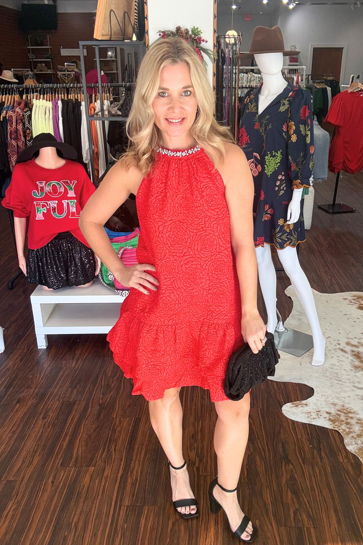 Elevate your evening look with this striking red mini dress. The textured woven fabric creates visual depth, while the halter neckline showcases a stunning jewel embellishment for added glamour. Playful double ruffles at the hem add movement and dimension, and the back neck button closure ensures a secure, flattering fit. Perfect for cocktail events or nights out, this dress balances sophistication with contemporary edge