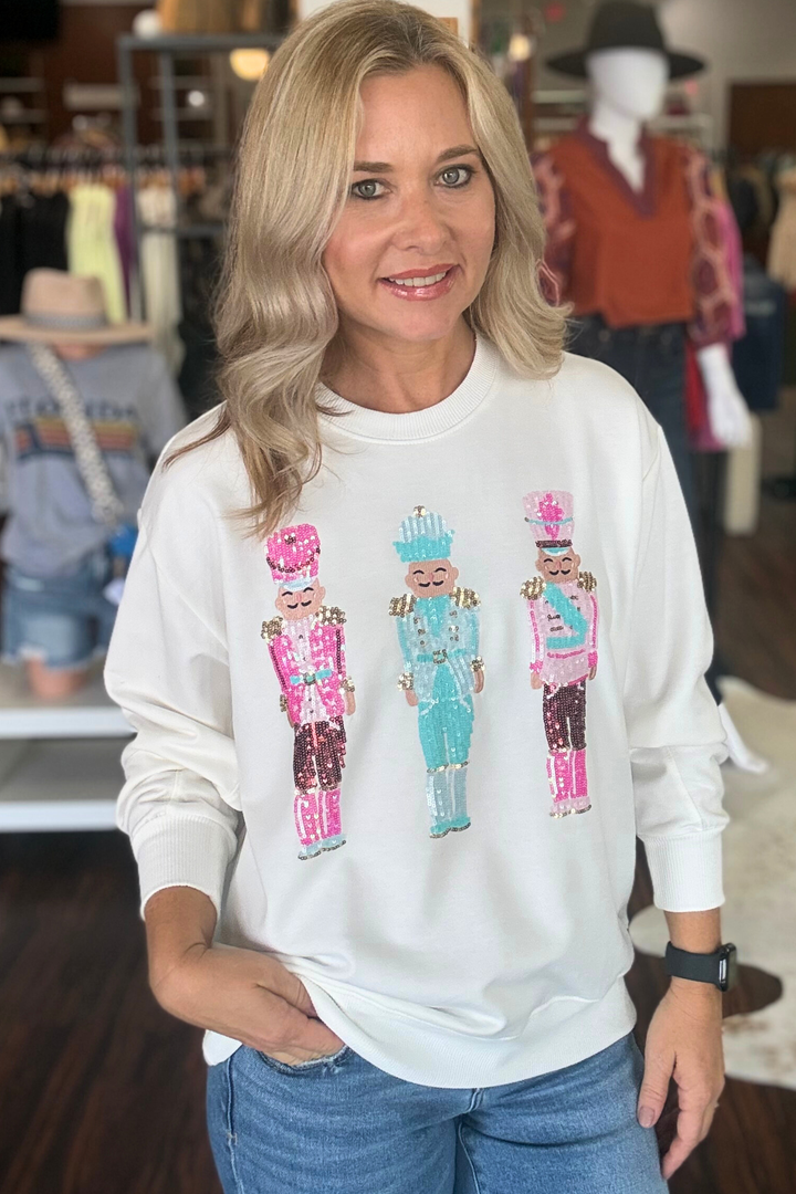 This white soft sweatshirt features three sequin Nutcrackers across the front, blending festive charm with comfortable wear. Its cozy fabric makes it perfect for cool days, while the sparkling details add a playful, modern twist 