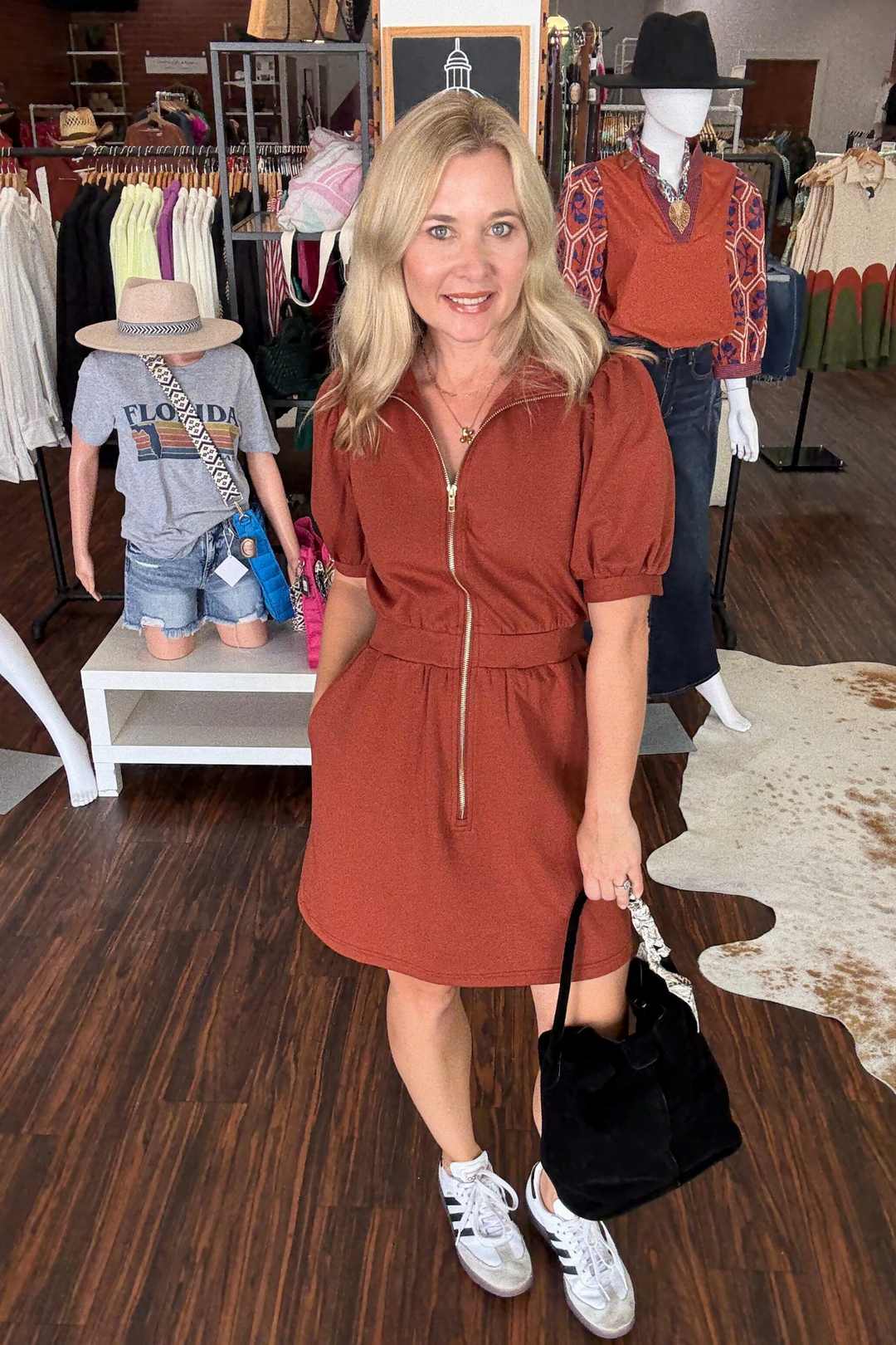 Woman in a rust-colored dress standing in a store with mannequins and clothing in the background