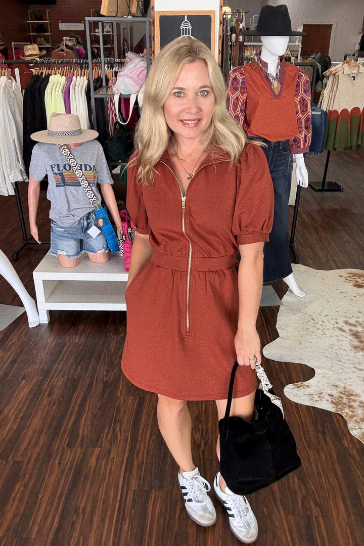 Woman in a rust-colored dress standing in a store with mannequins and clothing in the background